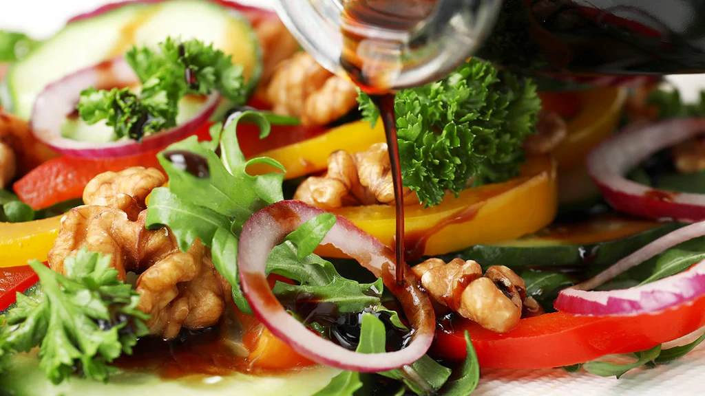 A small bowl of glossy maple balsamic dressing with a whisk